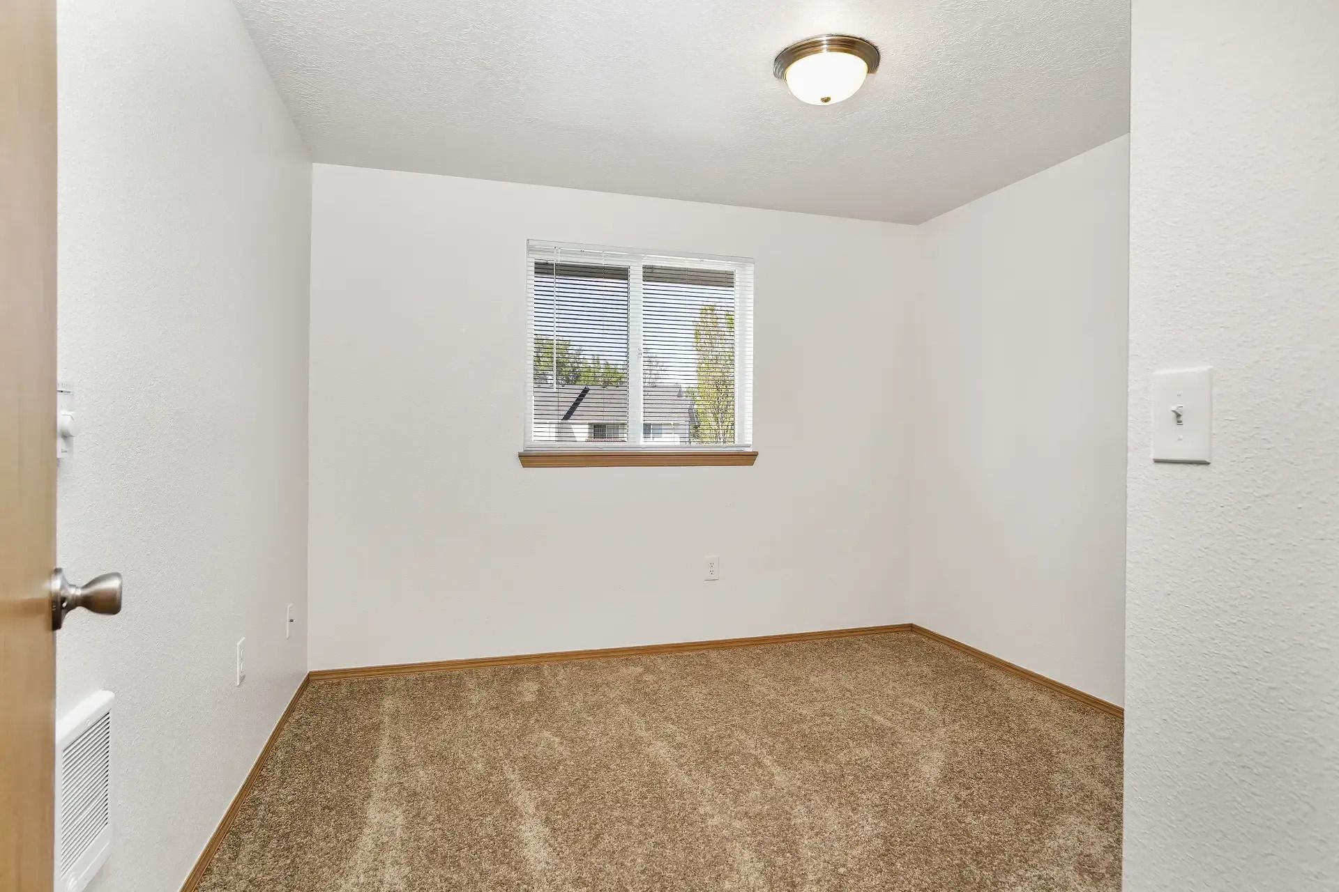 Small empty room with white walls, beige carpet, and a window with blinds.