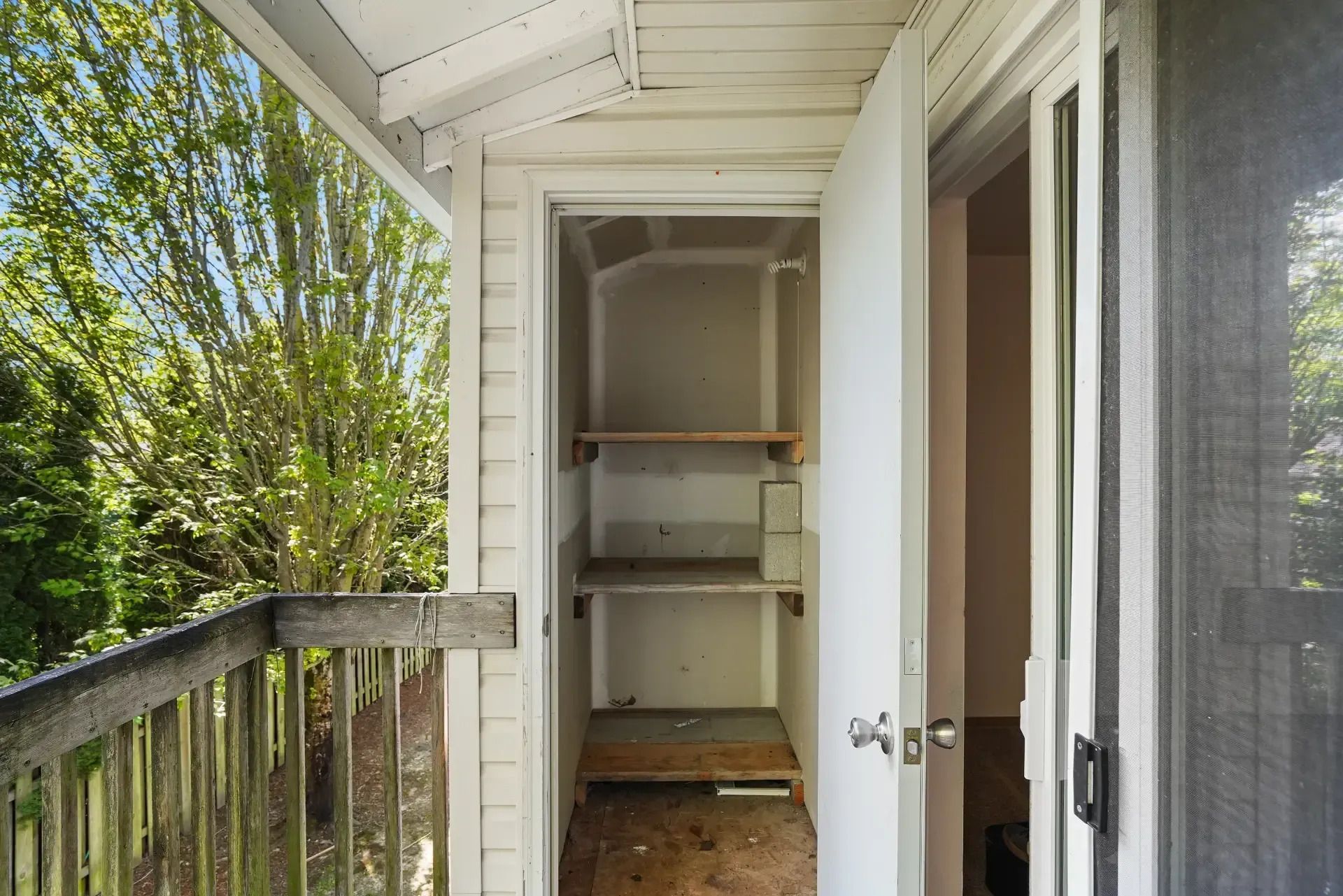 Small outdoor closet with shelves and a wooden floor beside a balcony doorway