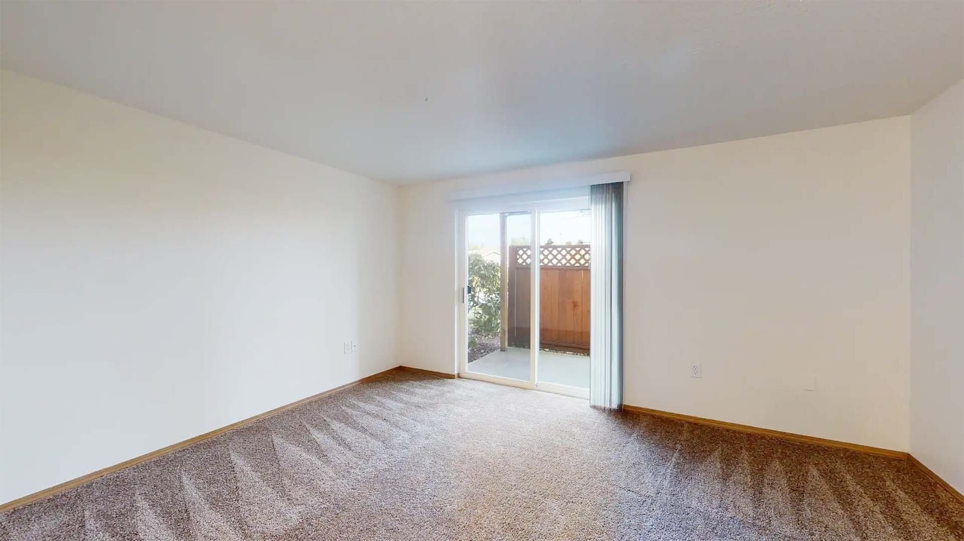 Empty carpeted bedroom with white walls and sliding glass door to a balcony or patio.