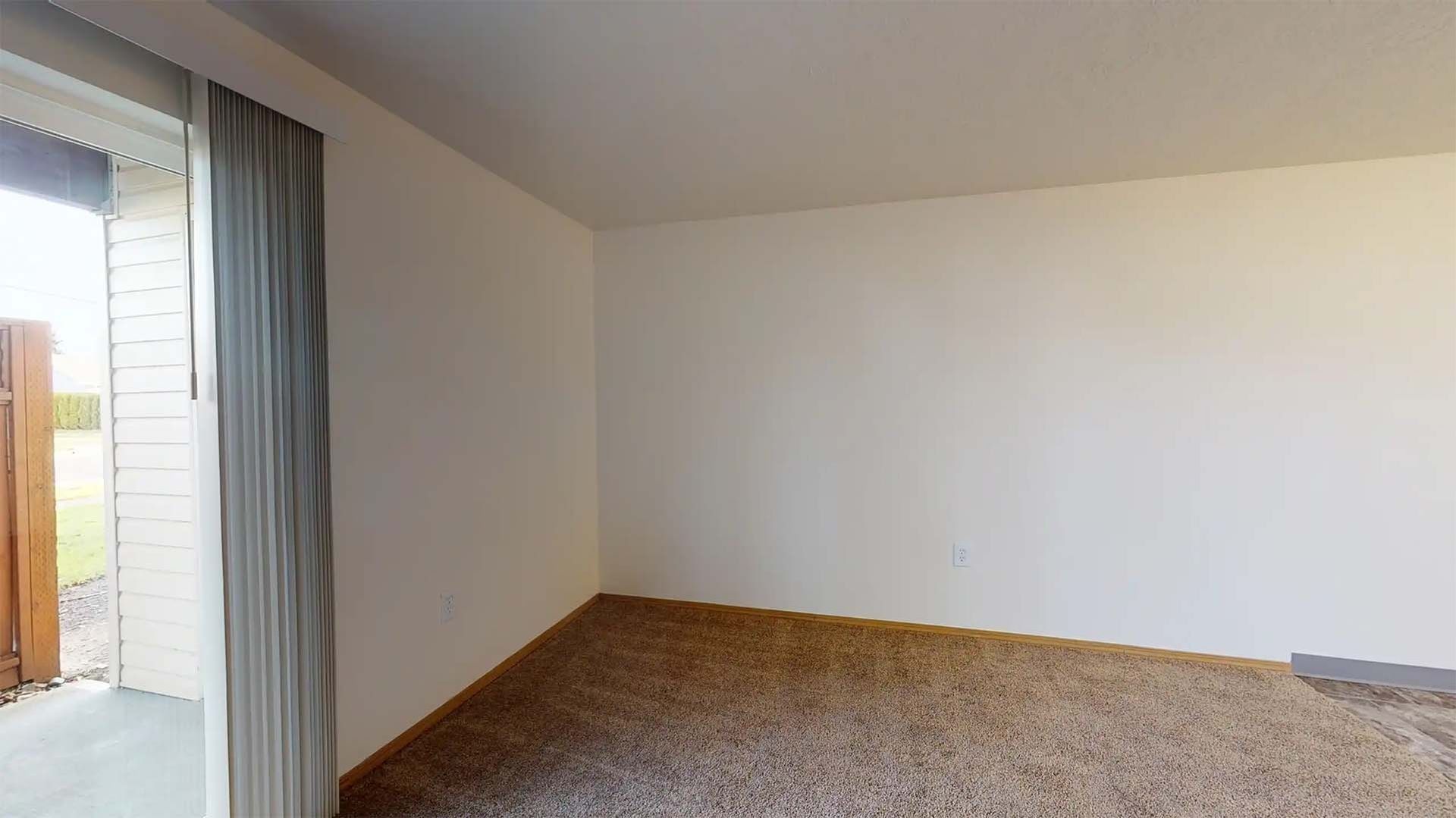 Empty carpeted room with white walls, sliding glass door, and gray curtains.