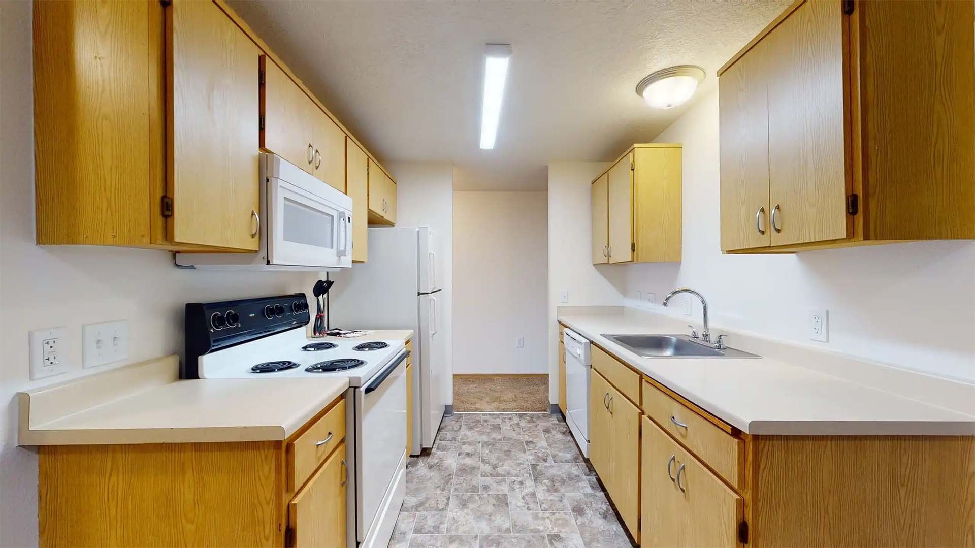 Bright galley kitchen with white appliances, wood cabinets, and tiled floor