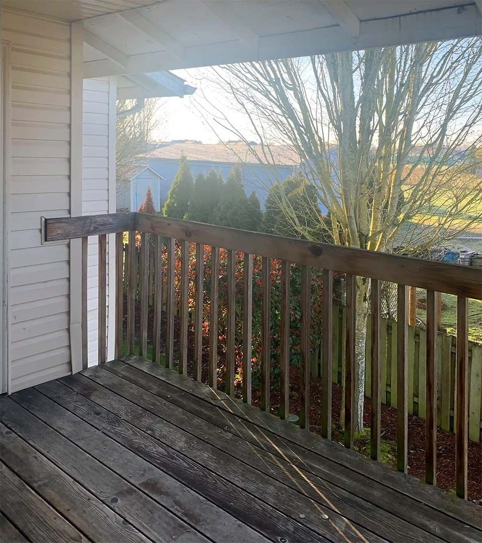 Wooden deck with railing beside a house, overlooking trees and distant mountains in morning light