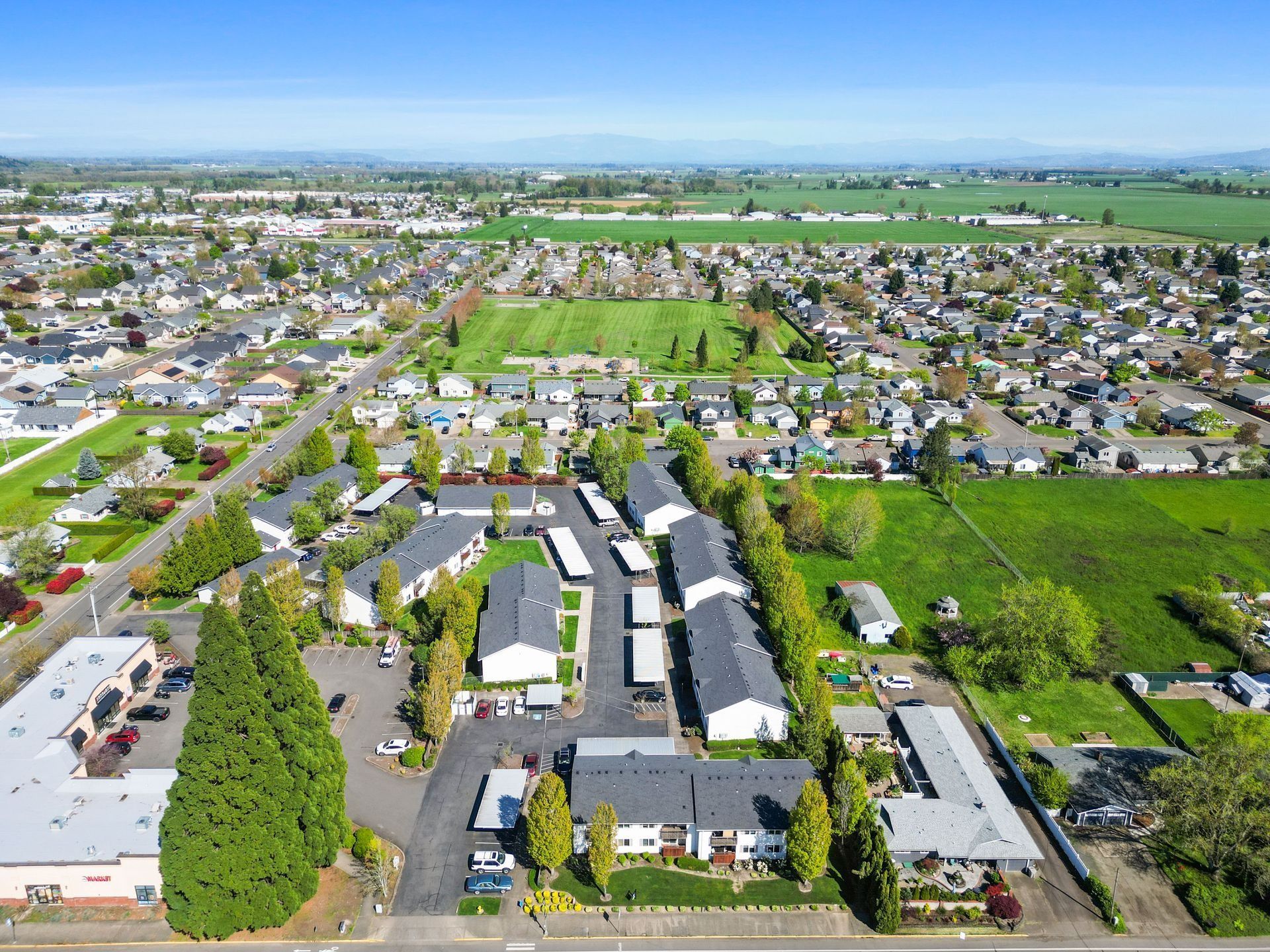 Aerial view of a suburban neighborhood with houses, roads, green fields, and open land