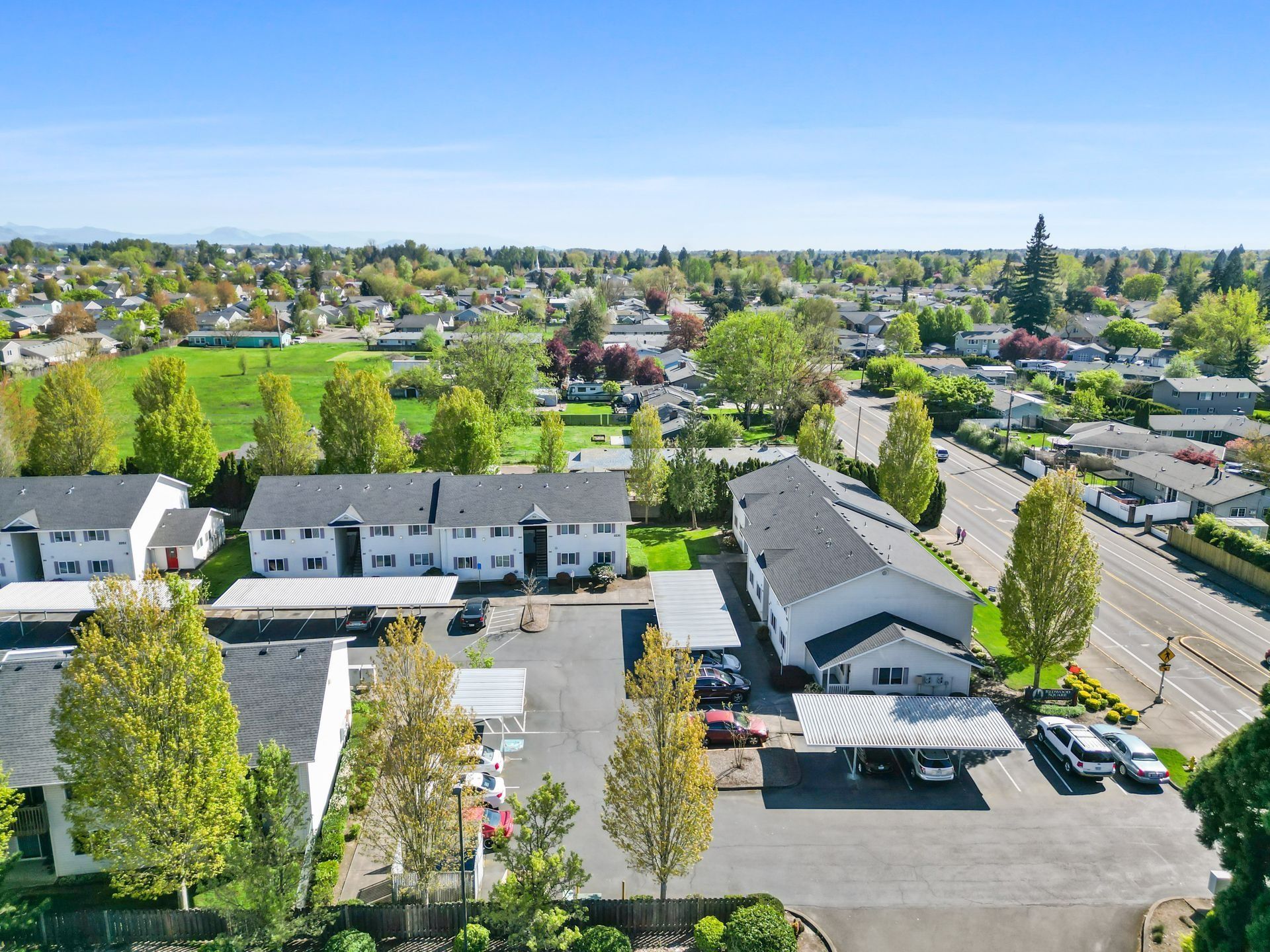 Aerial view of a suburban neighborhood with houses, trees, and roads under a clear blue sky
