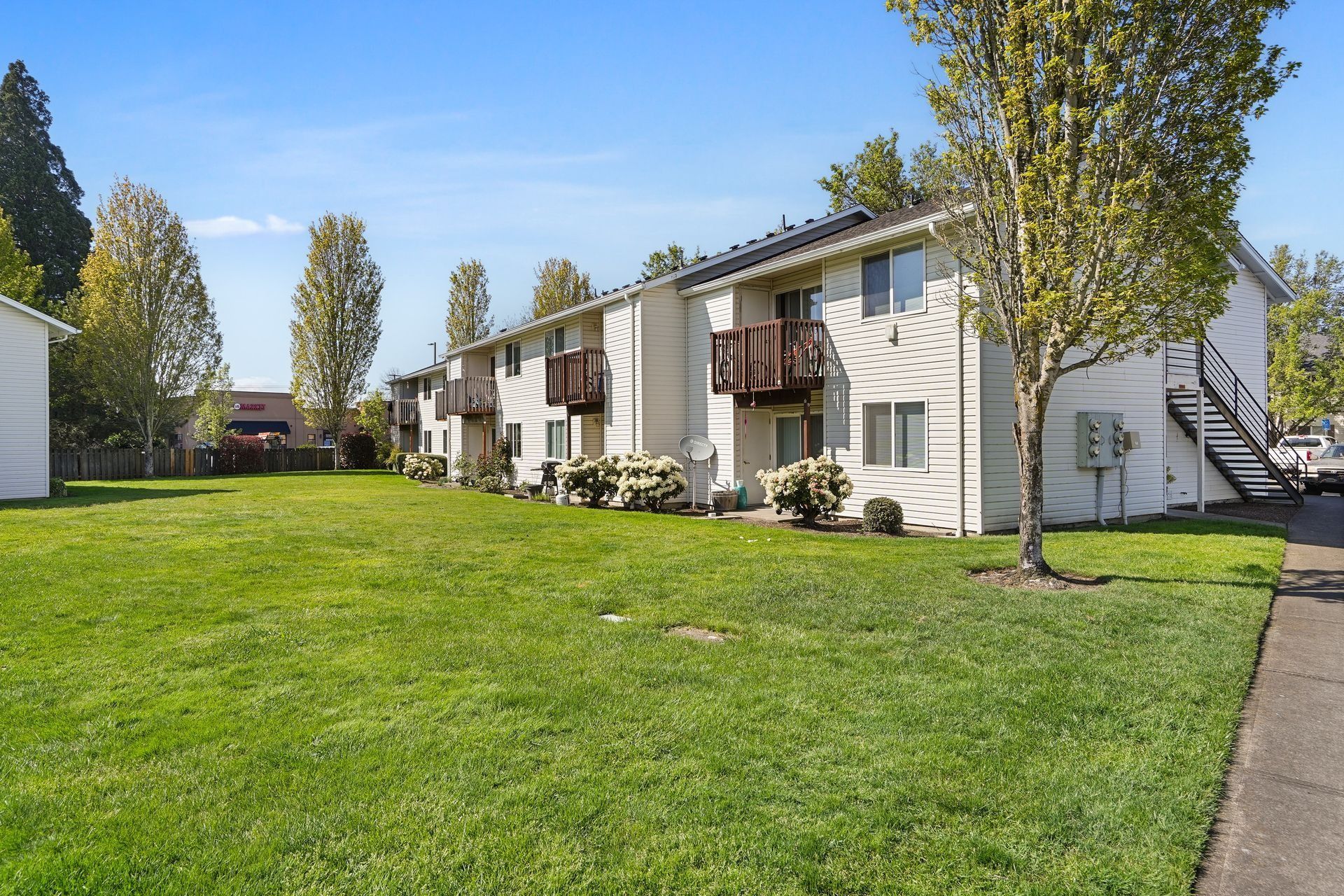 Apartment buildings with balconies beside a green lawn and sidewalk on a sunny day