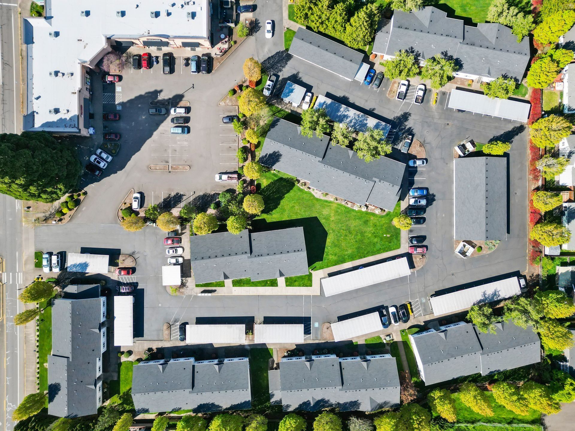 Aerial view of a residential apartment complex with parking lots, roads, and surrounding trees.