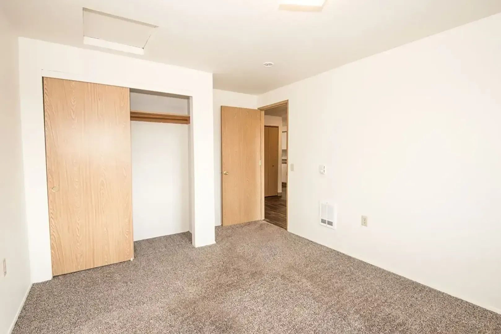 Empty carpeted bedroom with white walls, two open closets, and a doorway