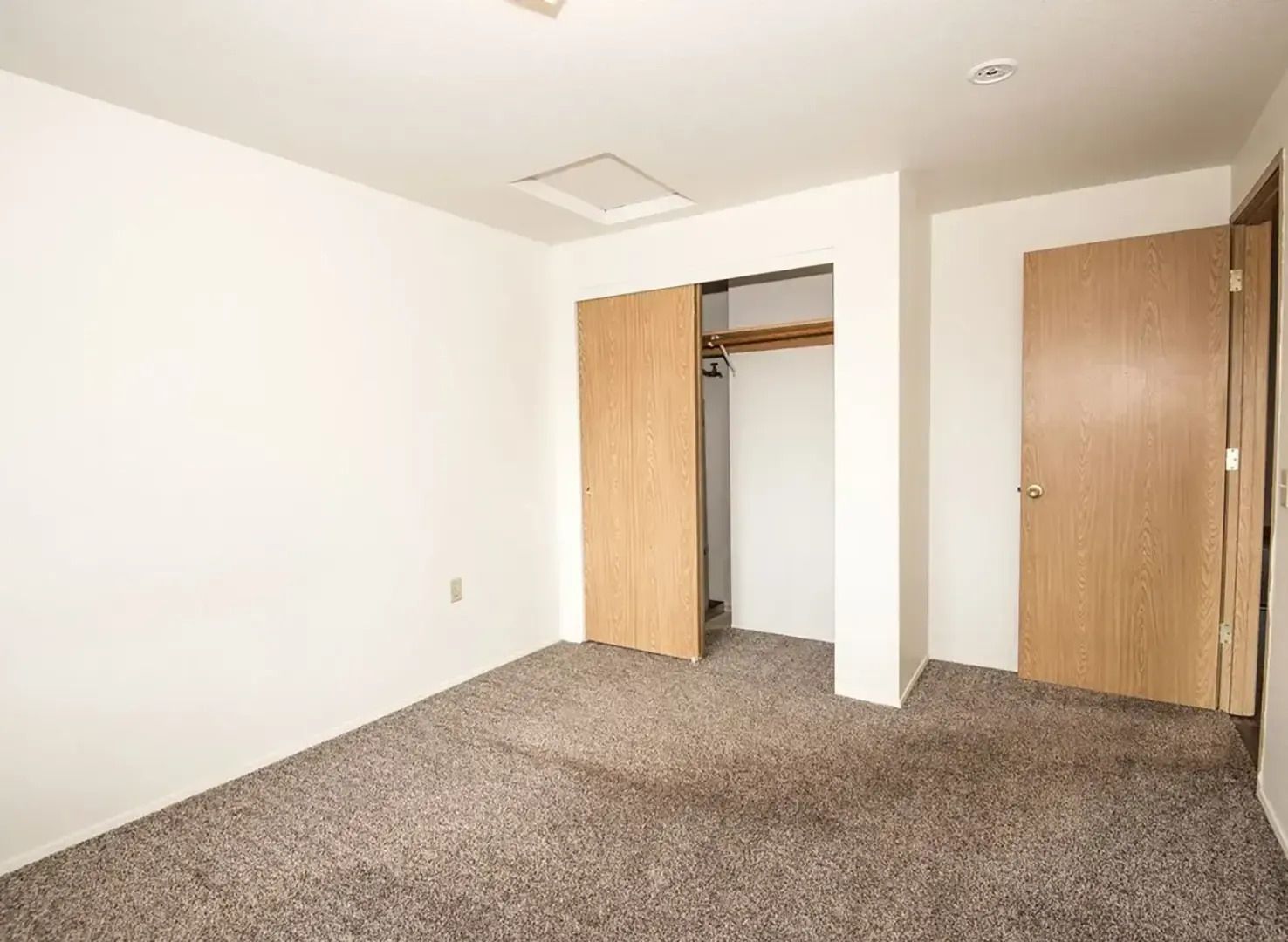 Empty beige bedroom with open closet doors and carpeted floor