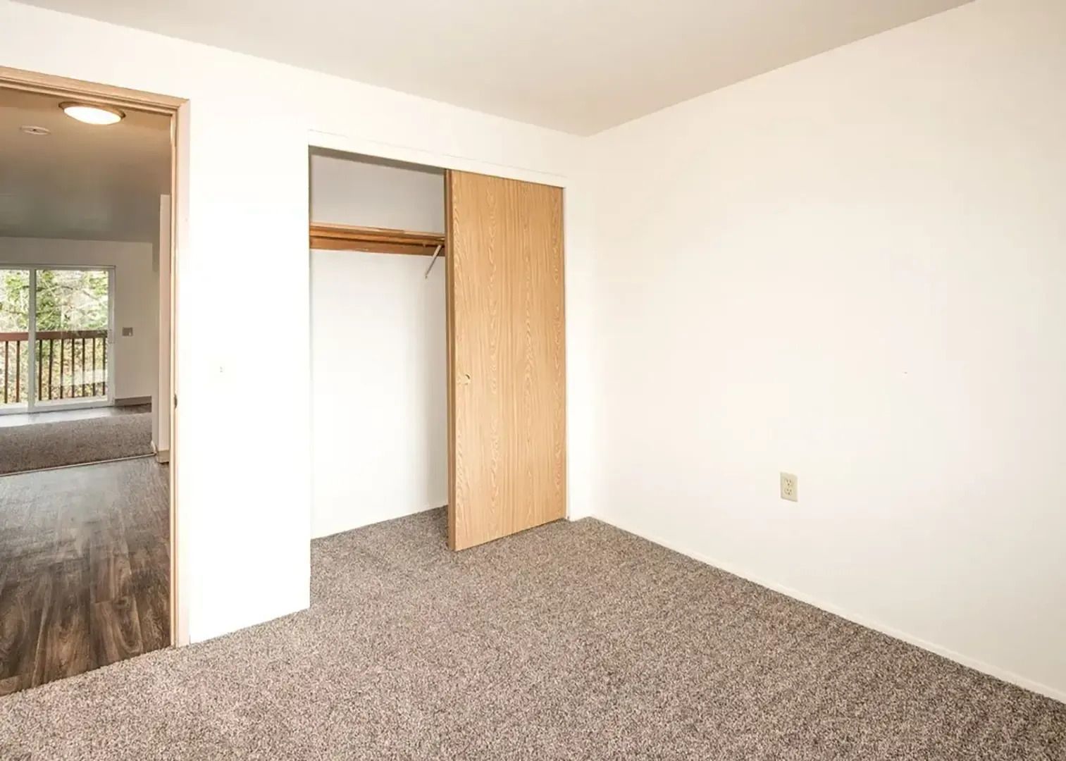 Empty carpeted bedroom with open closet and doorway to a hallway