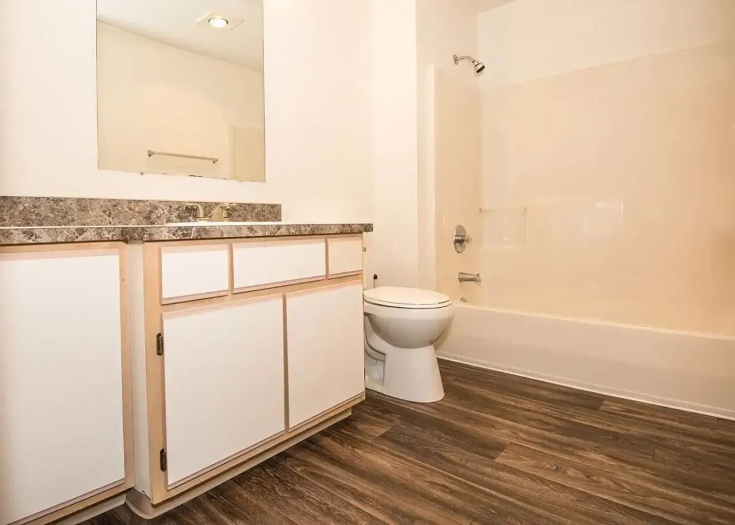 Modern bathroom with white vanity, toilet, beige walls, and wood-look flooring
