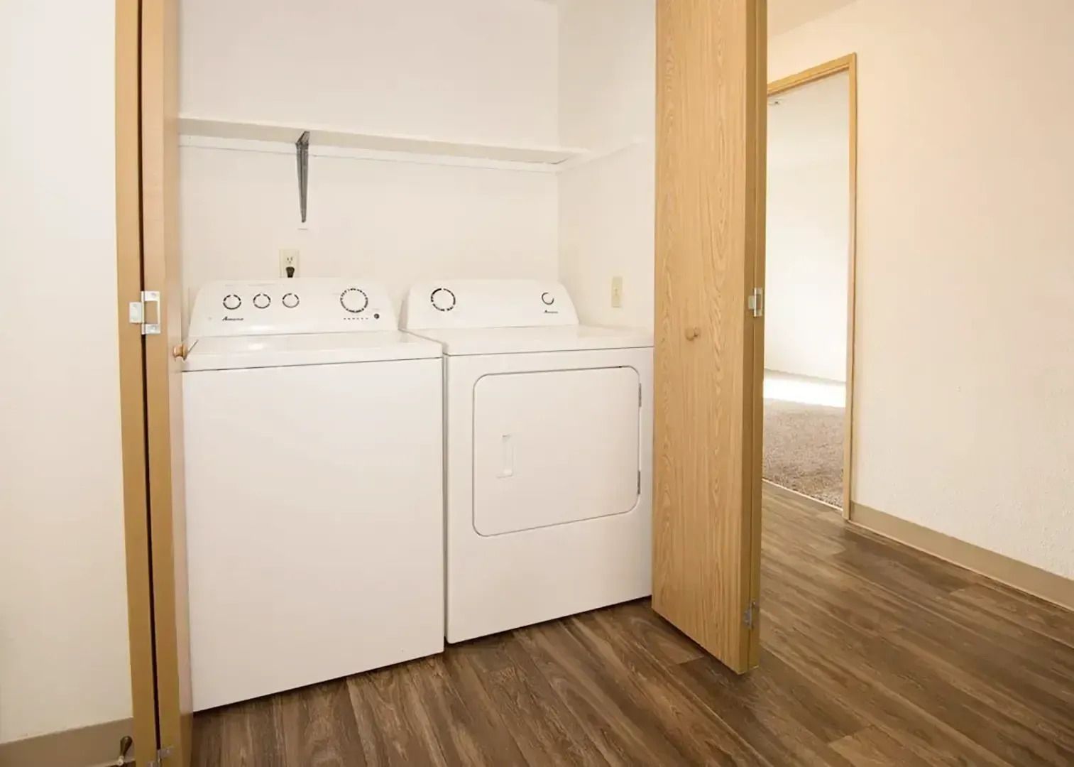 Laundry area with white washer and dryer in a small closet, wood floors and open door.