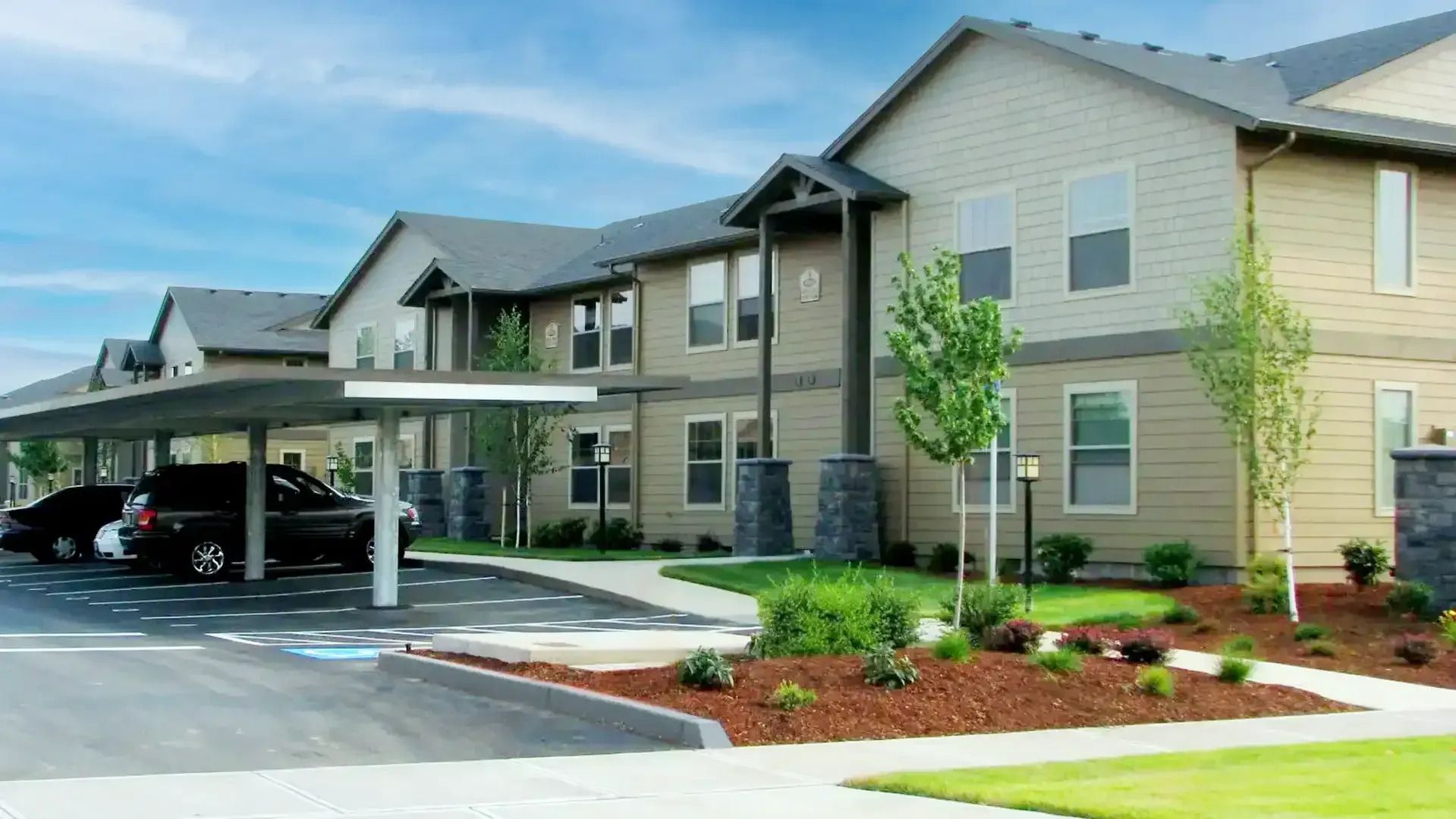 Apartment complex with covered parking and landscaped walkways under a clear sky