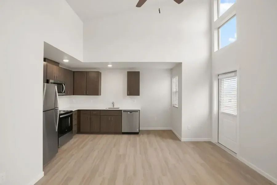 Bright empty apartment kitchen and living area with wood floors, white walls, and high ceilings