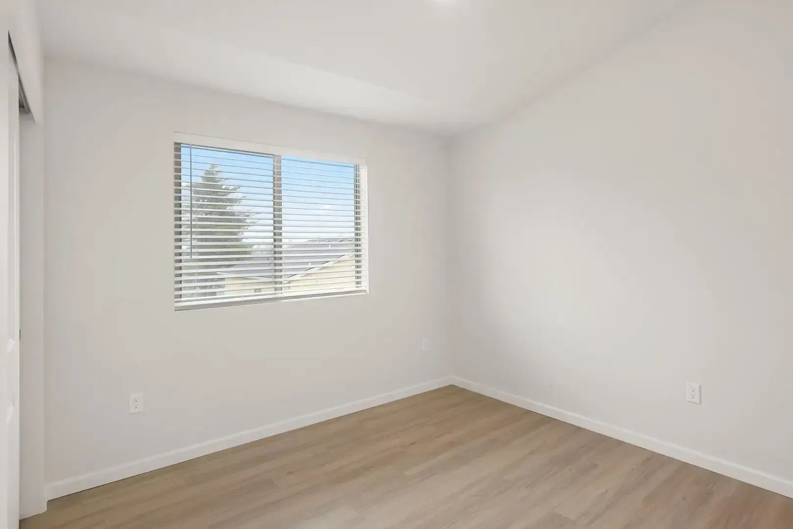Empty white bedroom with wood floor and a window with blinds