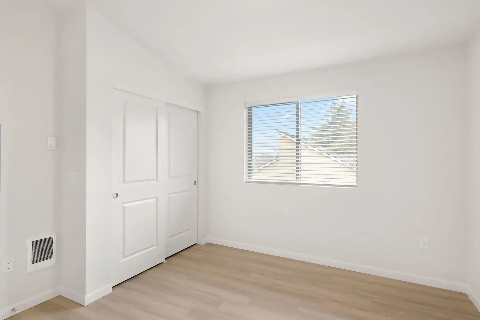Empty white bedroom with closet, window blinds, and light wood floor
