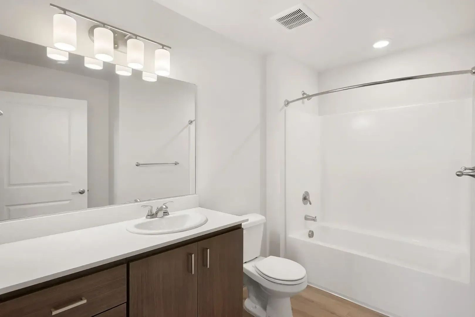 Modern bathroom with white tub-shower, toilet, vanity, and vanity lights