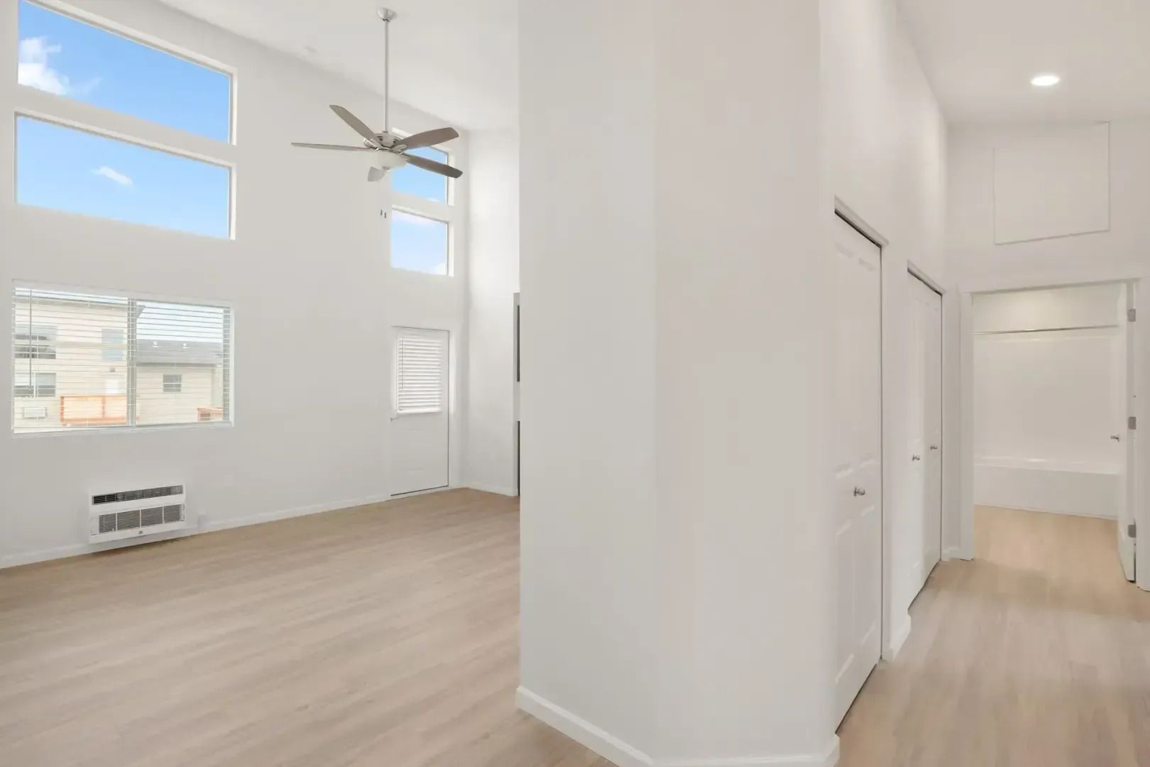 Bright, empty open-plan home interior with high ceilings, wood floors, and a hallway to the right