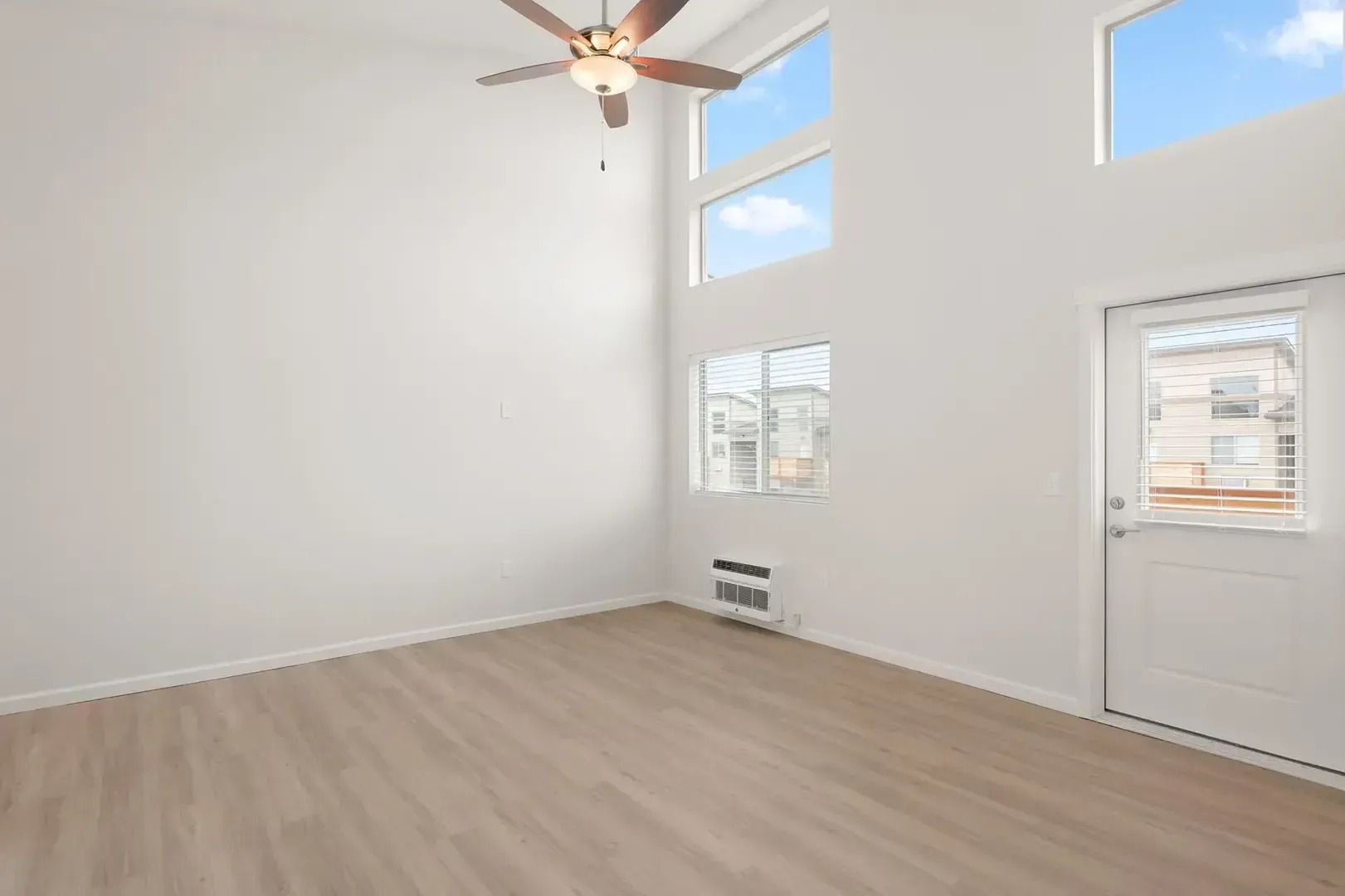 Empty bright room with high ceilings, large windows, light wood floor, and ceiling fan.