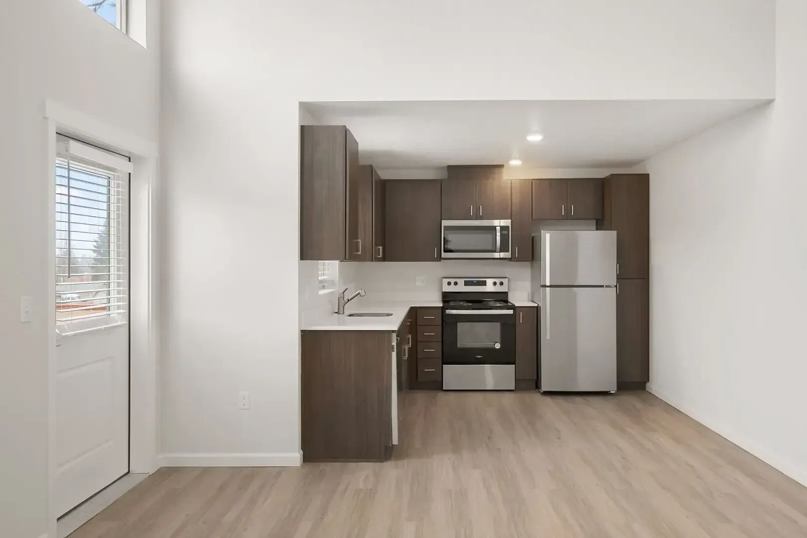 Modern empty kitchen with stainless steel appliances, wood cabinets, and light wood flooring