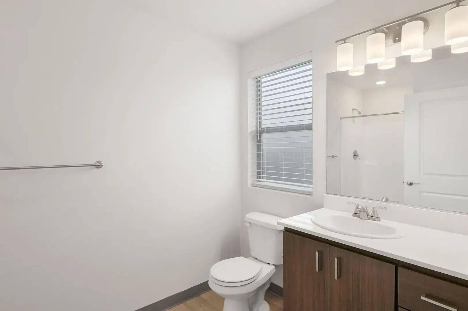 Modern bathroom with white walls, vanity mirror lights, toilet, and window blinds