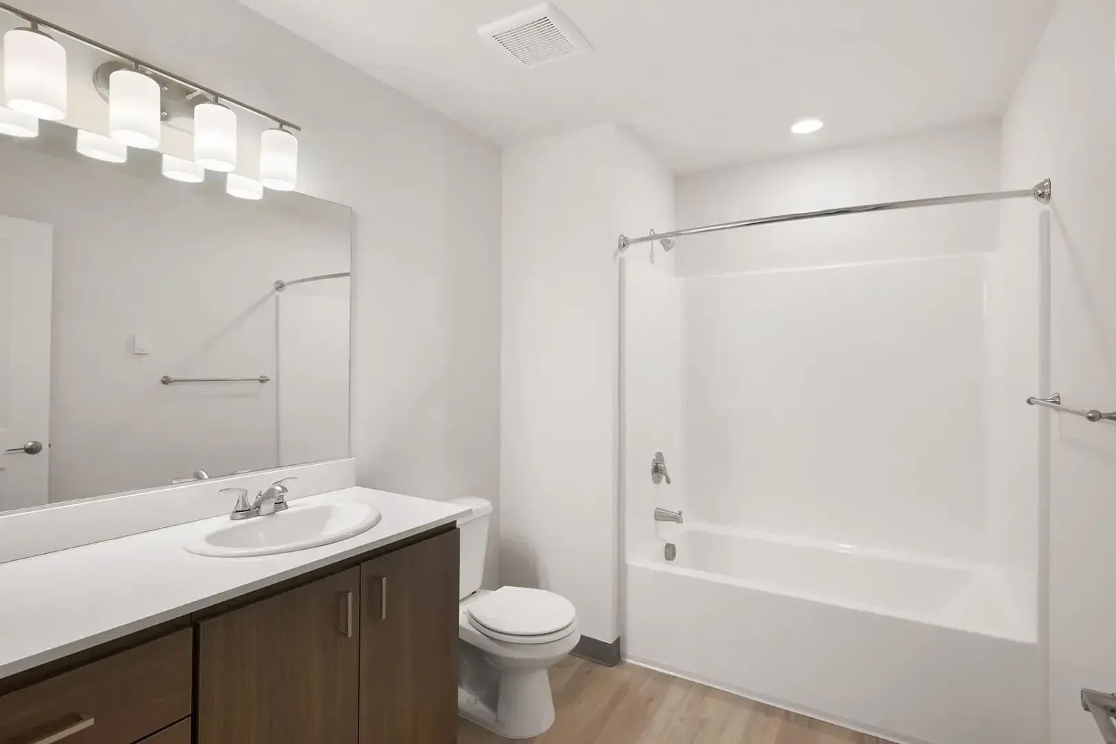 Modern bathroom with white tub, vanity, mirror, and wood flooring