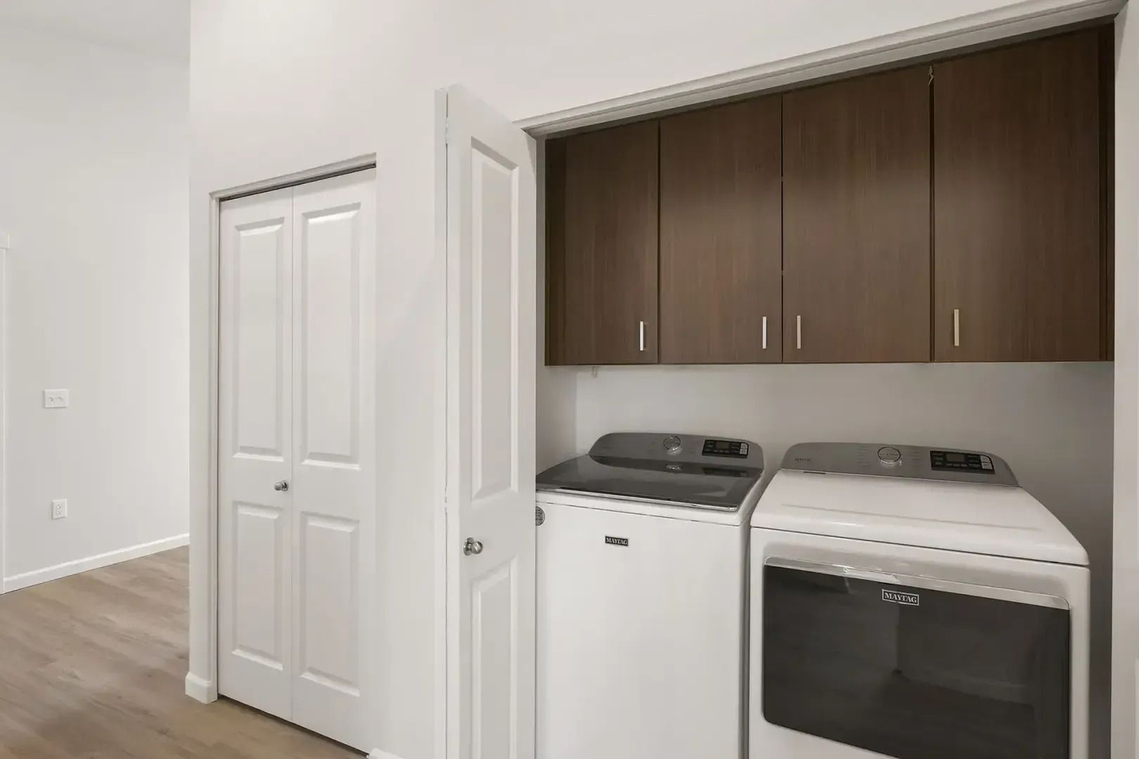 Laundry room with white washer and dryer, brown cabinets, and a closed closet door