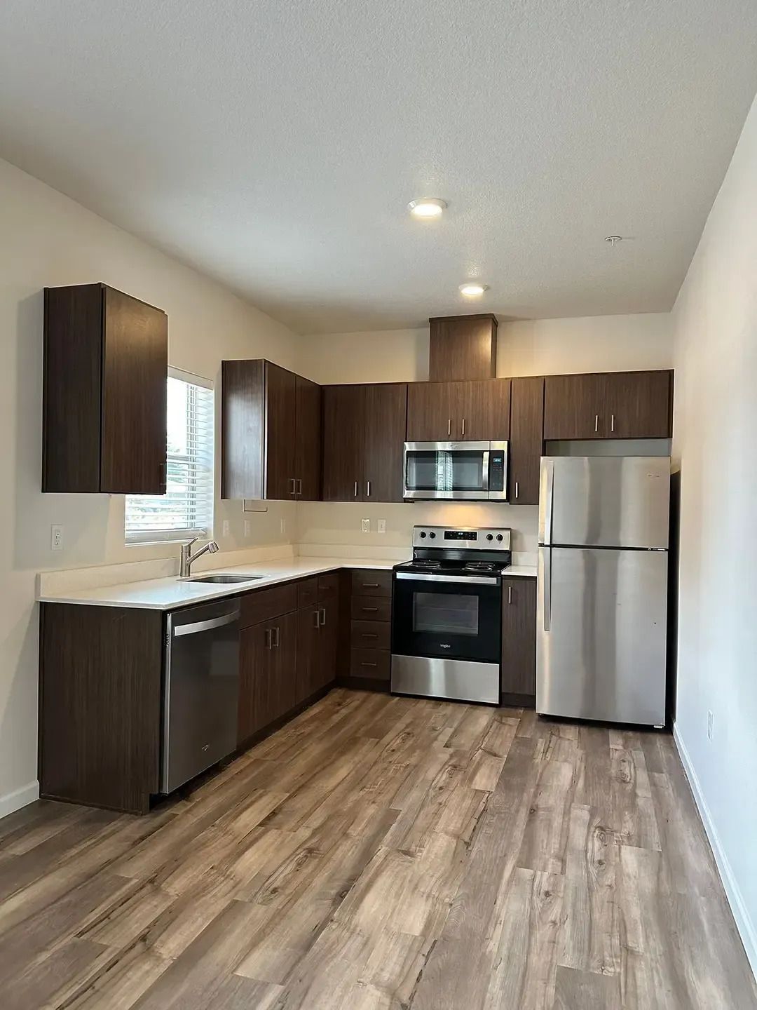 Small modern kitchen with dark wood cabinets, stainless steel appliances, and wood-look flooring