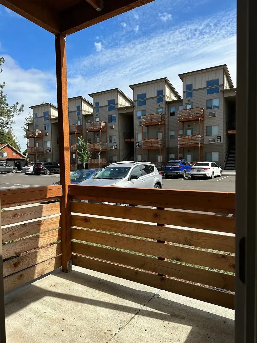 View from a wooden porch toward parked cars and modern apartment buildings on a sunny day