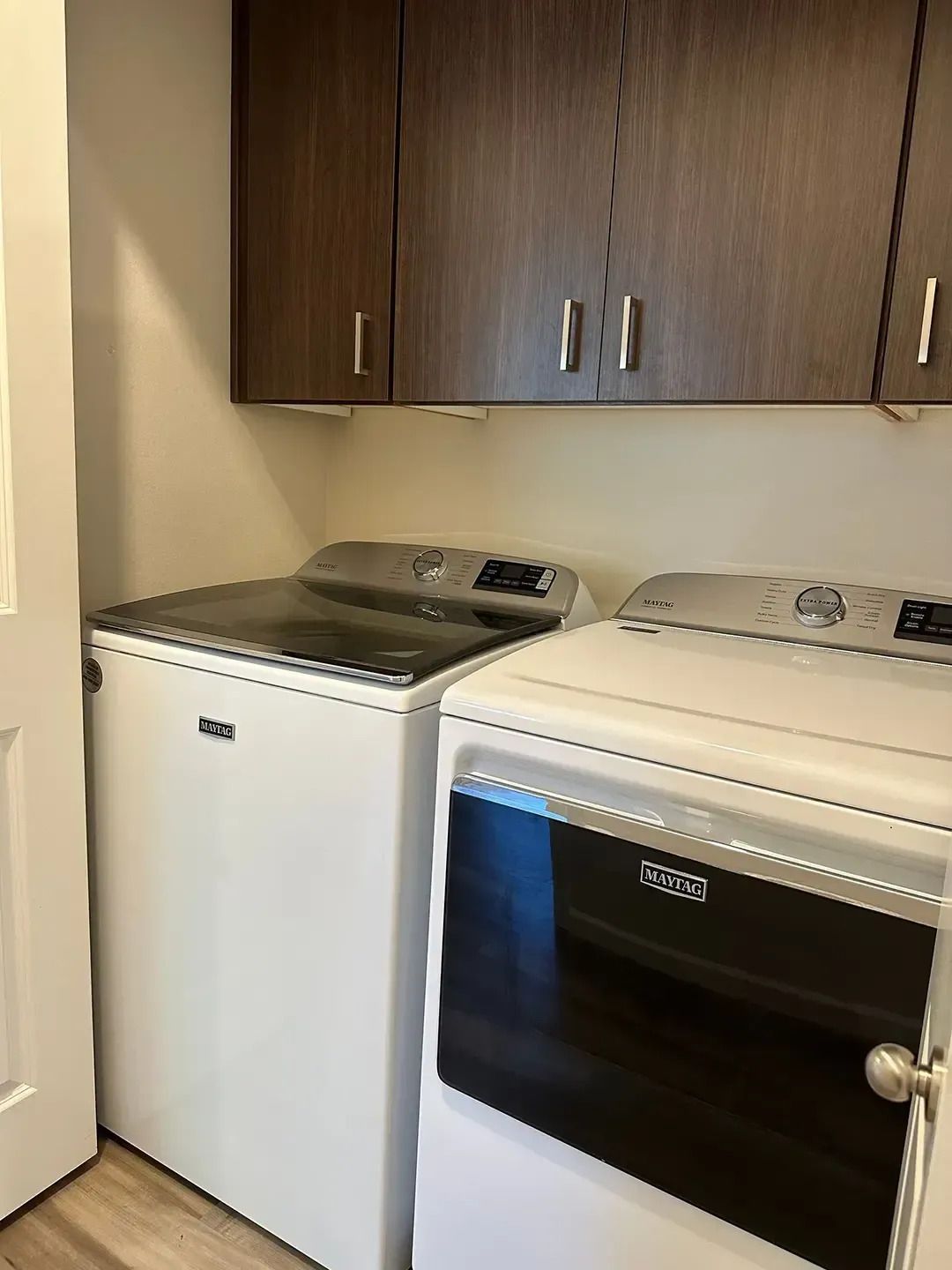 Laundry room with a white washer and dryer under dark wood cabinets.