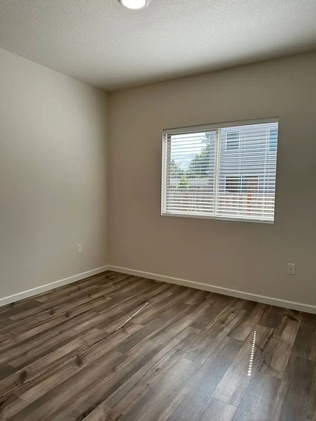 Empty room with gray walls, wood-look flooring, and a window with blinds.