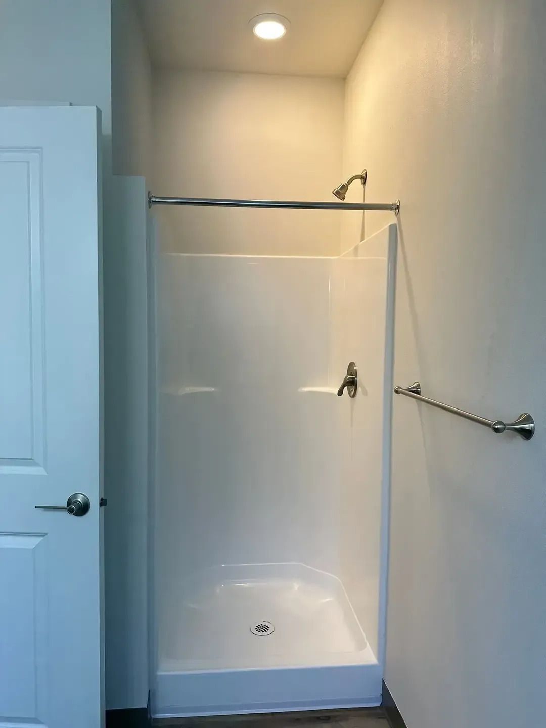 Small bathroom shower stall with clear glass, white walls, and a chrome grab bar.