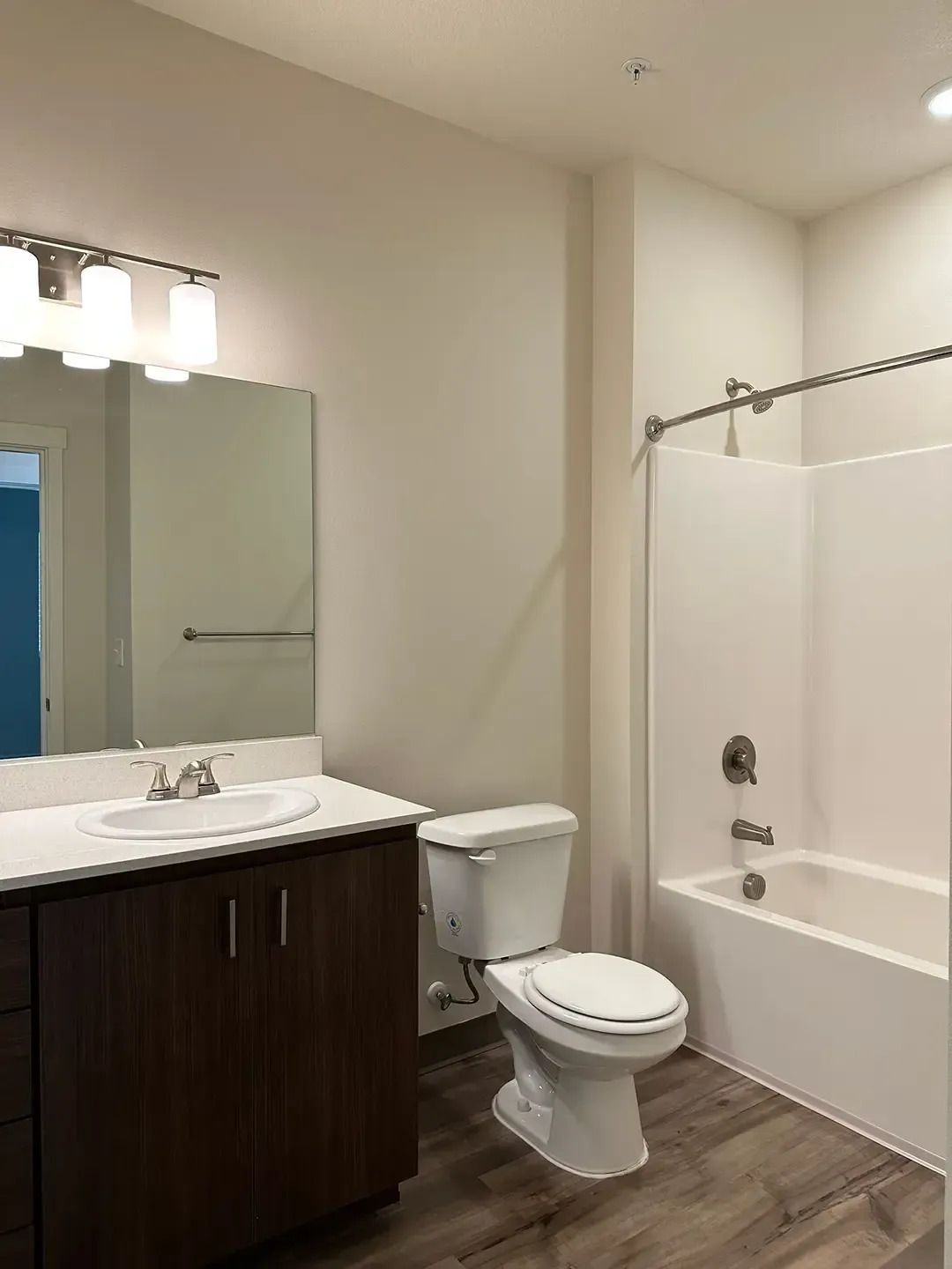 Small bathroom with dark vanity, white tub-shower, toilet, and mirror under three-light fixture.