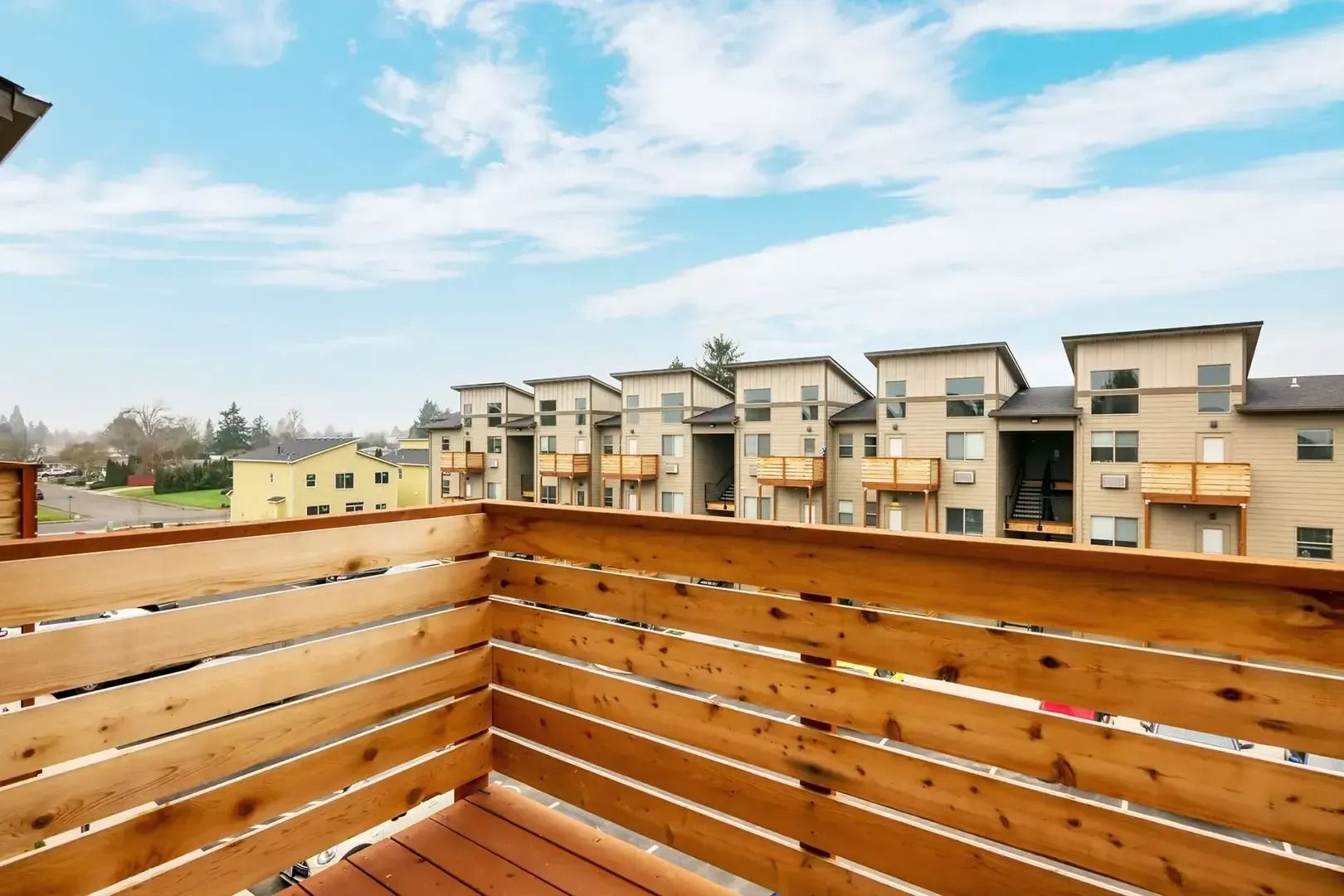 Wooden balcony deck overlooking modern apartment buildings under a blue sky