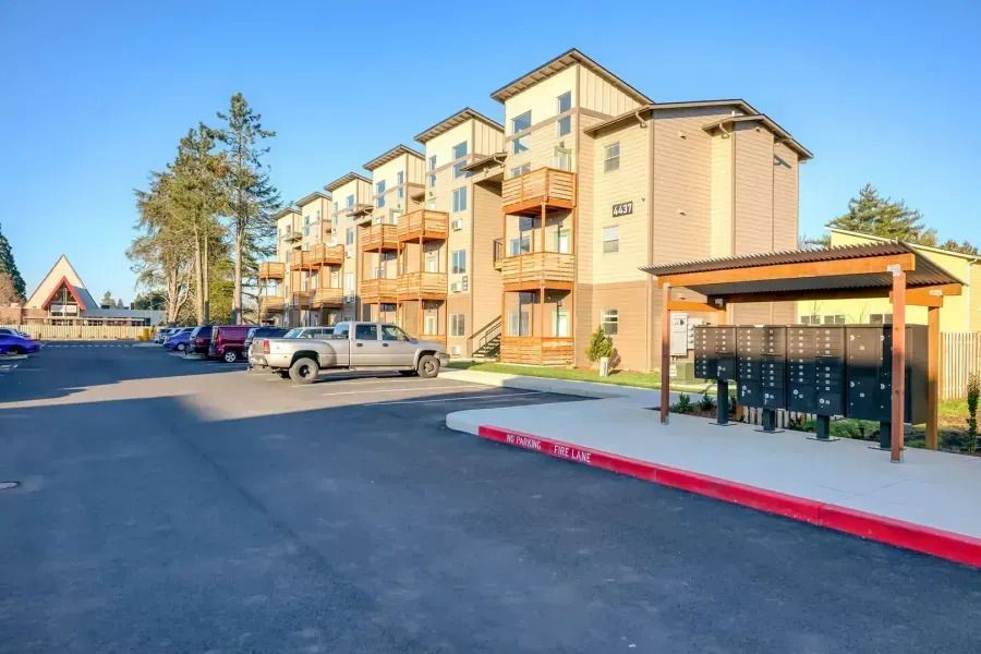 Apartment building parking lot with cars and a covered trash enclosure in sunlight