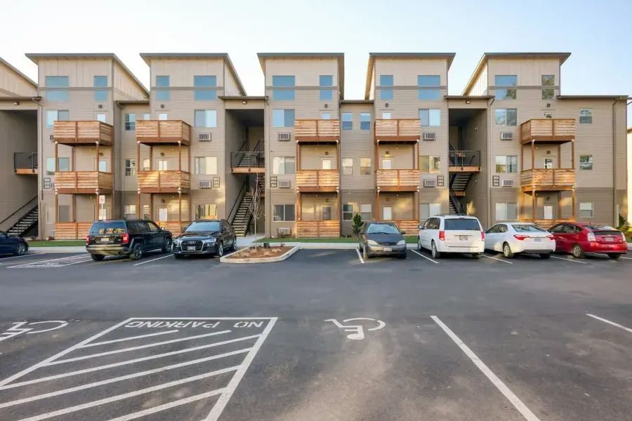 Apartment building with parked cars in front, seen across a marked parking lot at dusk