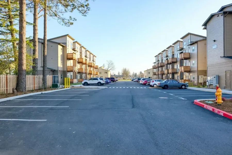 Apartment complex parking lot with parked cars, townhomes, and trees on a clear day
