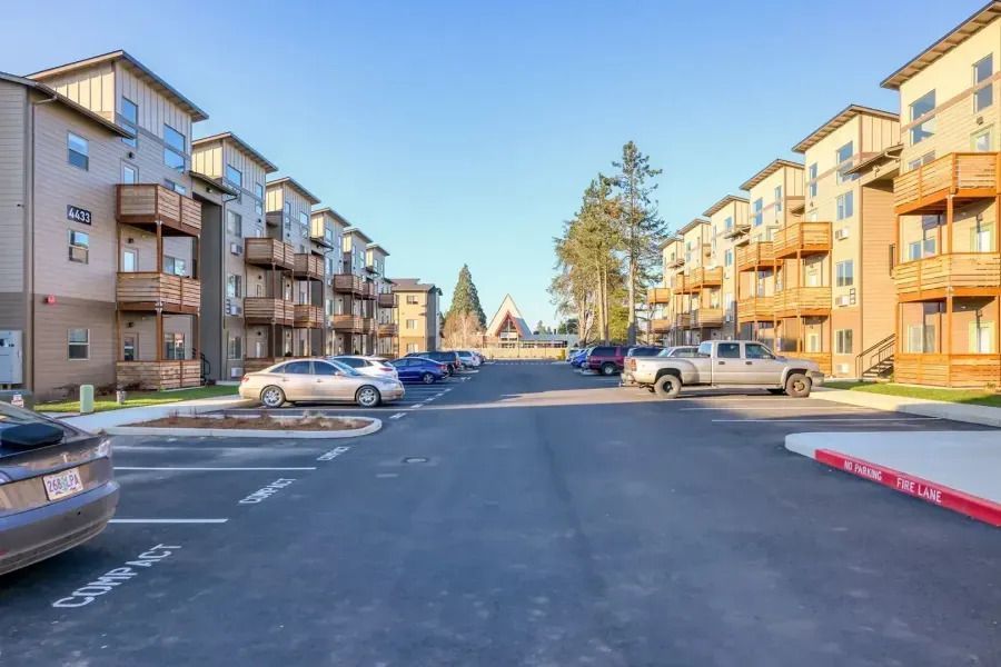Apartment complex parking lot with parked cars on a sunny day, viewed down a central driveway