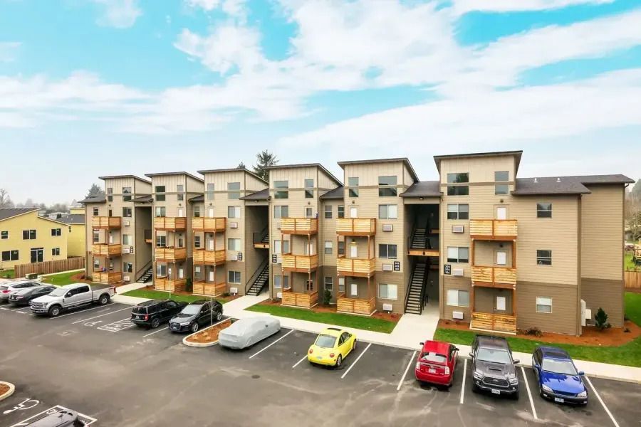 Apartment complex with balconies and parked cars in front under a partly cloudy sky