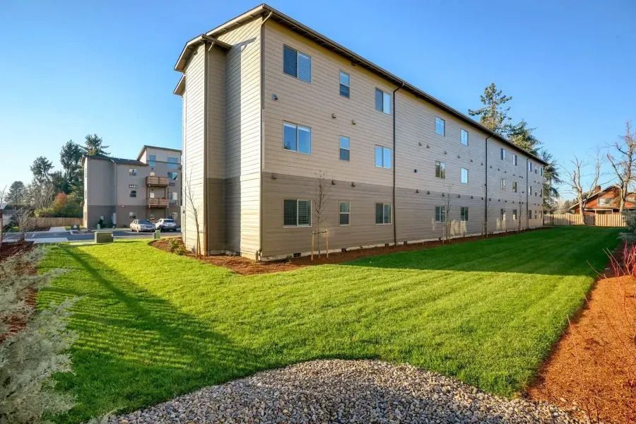 Apartment building with beige siding beside a green lawn under a bright blue sky