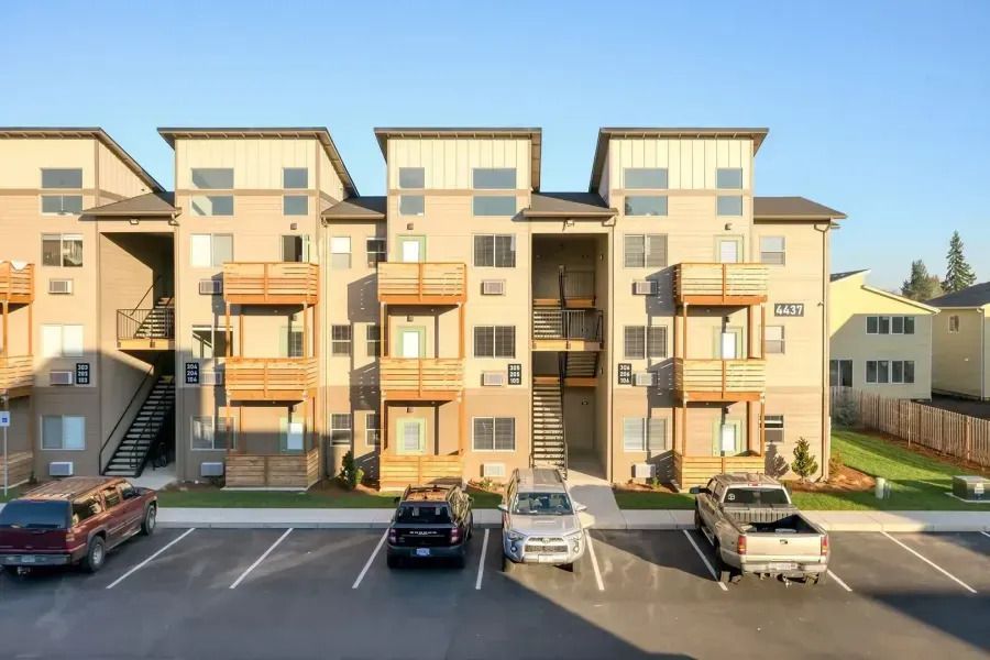 Three-story apartment building with parked cars in front at sunset