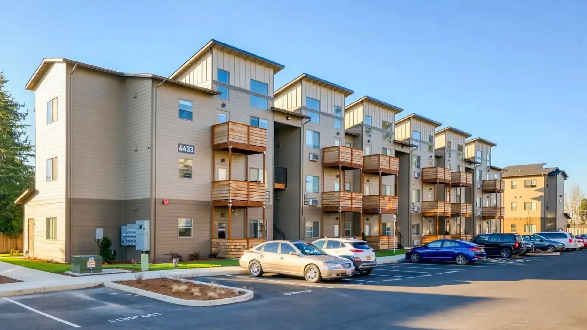 Apartment complex with beige buildings, parked cars, and balconies under a clear blue sky