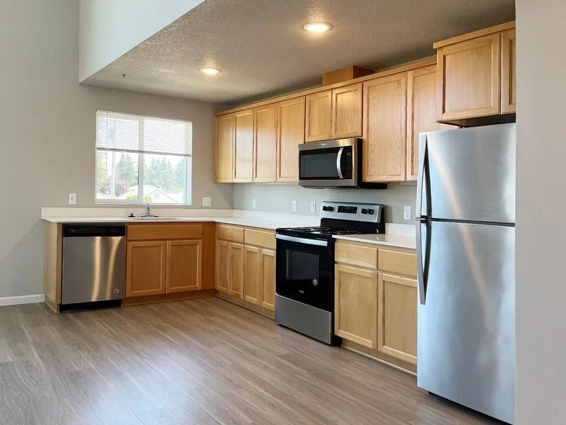 Modern kitchen with light wood cabinets, stainless steel appliances, and a window over the sink