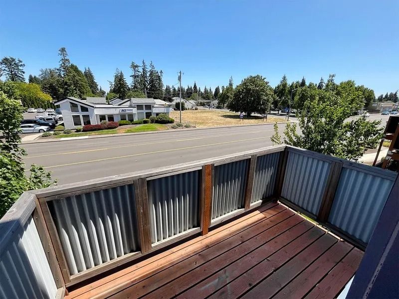 Wooden deck overlooking a street and houses, with gray railings and trees in the background
