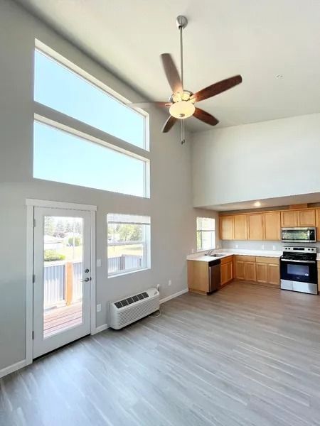 Bright open kitchen and living area with high windows, ceiling fan, and light wood flooring