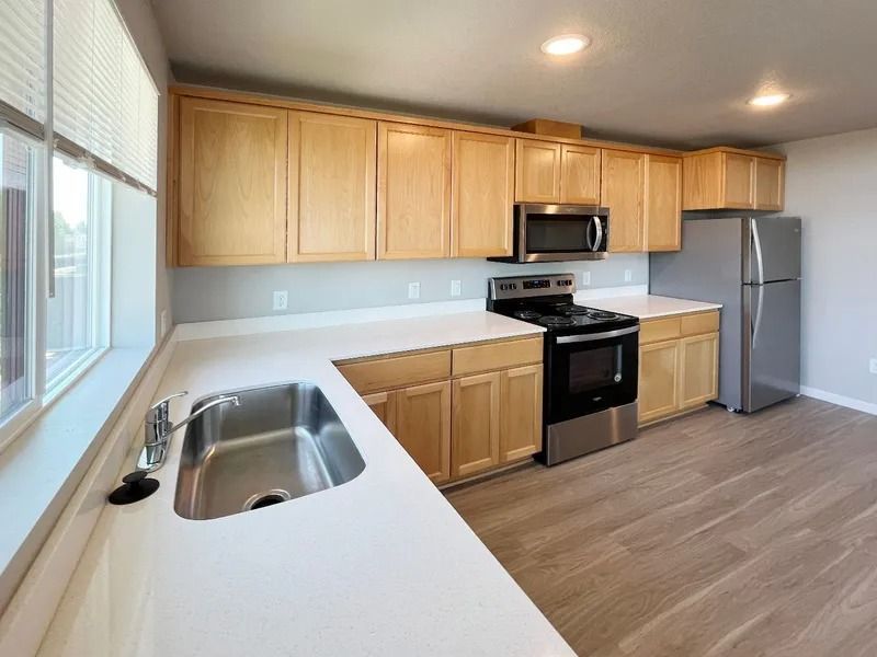 Modern kitchen with light wood cabinets, white countertops, stainless sink, black appliances, and gray flooring