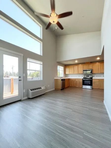 Bright open living room with vaulted ceiling, ceiling fan, wood floors, and small kitchen area.