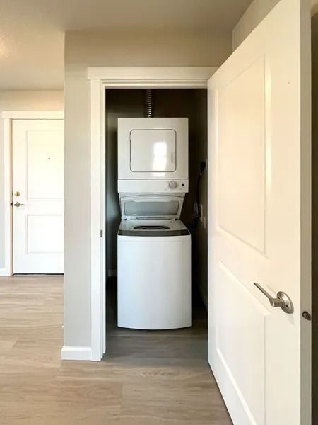 Hallway view of a stacked washer and dryer in a recessed laundry closet with white doors open.