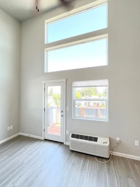 Empty bright room with tall windows, sliding glass door, and a wall-mounted air conditioner