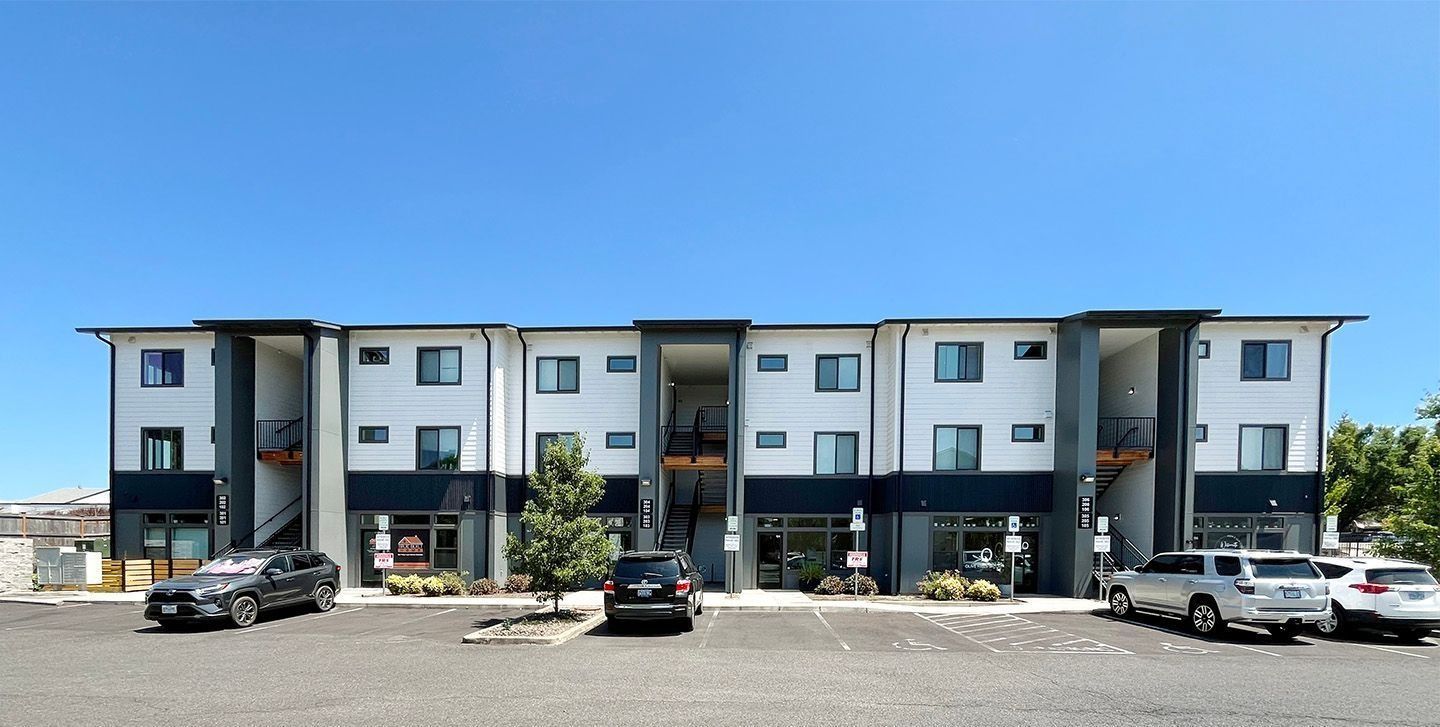 Three-story apartment building with parked cars in front on a sunny day