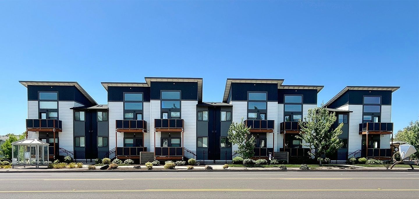 Modern row of blue-and-black townhouses with balconies along a street under clear daylight